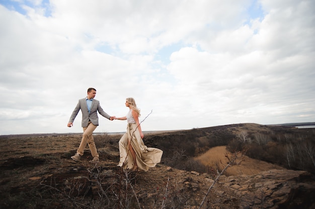 Handsome guy and blonde girl walking on the field, a man leads a woman holding the hand.