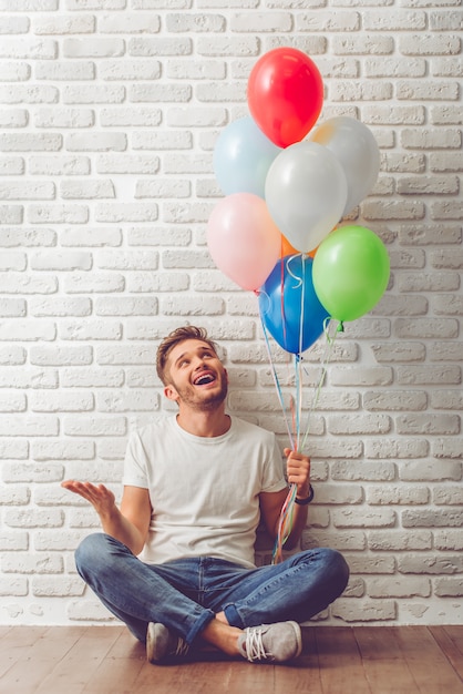 Handsome guy in casual clothes is holding balloons.