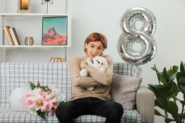 Handsome guy on happy women day holding teddy bear sitting on sofa in living room