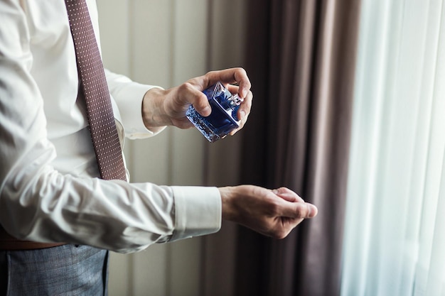 Handsome guy is choosing perfumes Elegant man in suit using colognegroom getting ready in the morning before wedding ceremony