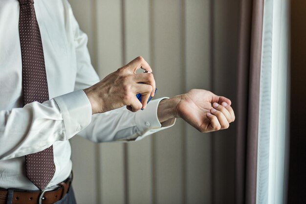 Handsome guy is choosing perfumes Elegant man in suit using colognegroom getting ready in the morning before wedding ceremony