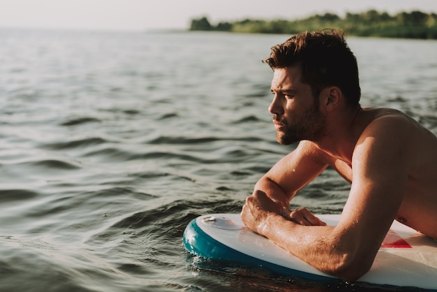 Handsome Guy Is Lays On Surf In The Water And Swims