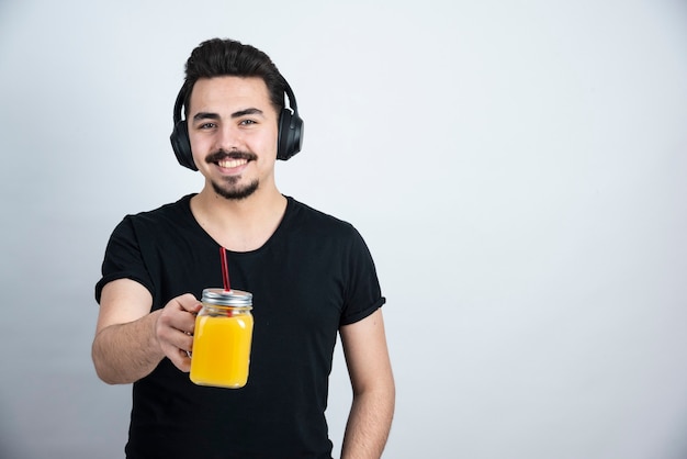 handsome guy model in headphones showing glass cup with orange juice to camera . 