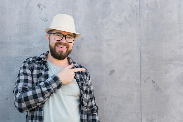 Handsome guy tourist looking happy wearing straw hat for travelling and pointing on empty space stan