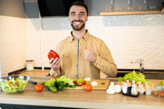 Handsome guy with beard and nice smile is giving a thumb on healthy lifestyle and eating fresh food.