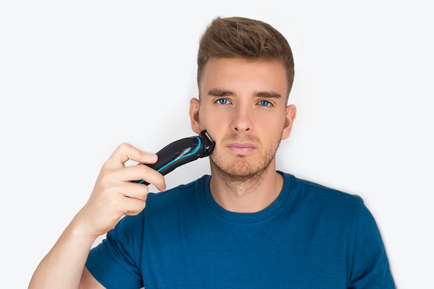 Handsome guy, young beautiful man shaving with an electric razor, trimming his beard, care for facial hair,  isolated on white . Beauty, men personal care. Hair clipper