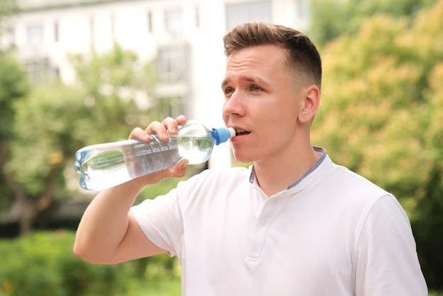 Handsome guy young happy thirsty man runner is drinking pure fresh water from plastic bottle