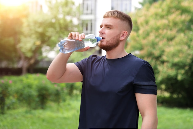 handsome guy young thirsty man runner is drinking fresh water from bottle after running jogging