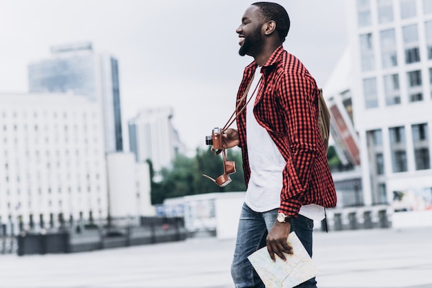 Handsome and happy Afro American tourist with old camera and map in modern city