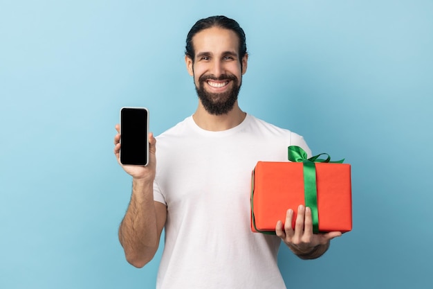 Handsome happy man holding gift box and cell phone with mock up blank display for advertise