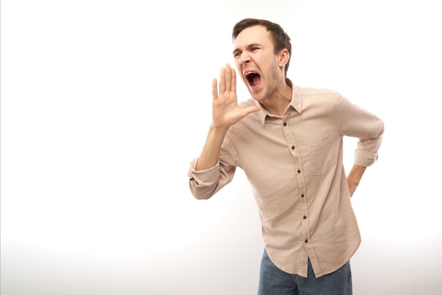 Photo handsome happy young caucasian male shouting and cupping hands around mouth isolated on white studio background. excited news attention!