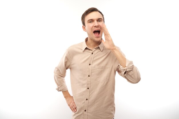 Handsome happy young caucasian male shouting and cupping hands around mouth isolated on white studio background. Excited news attention!