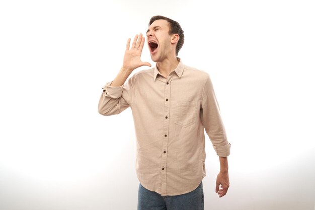 Photo handsome happy young caucasian male shouting and cupping hands around mouth isolated on white studio background. excited news attention!