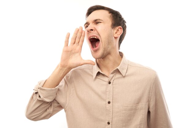 Photo handsome happy young caucasian male shouting and cupping hands around mouth isolated on white studio background. excited news attention!