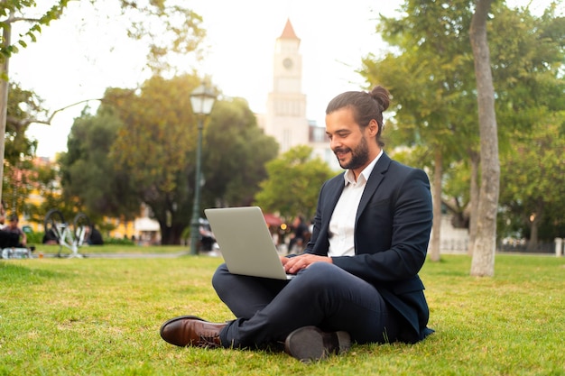 Handsome hispanic male businessman sitting lotus position in public park use laptop