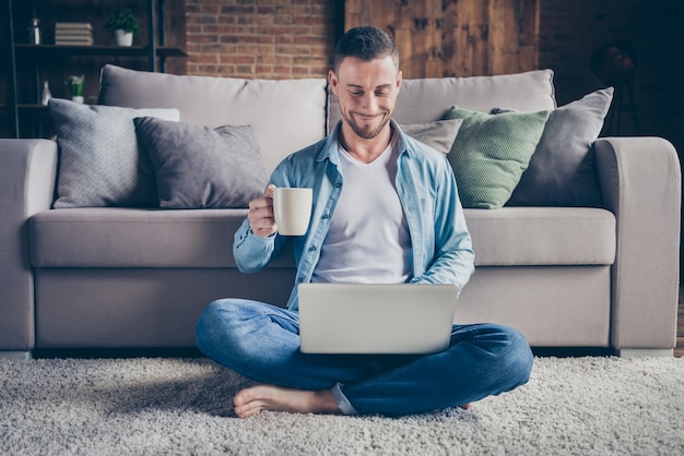 handsome homey guy relaxing sitting carpet drink coffee browsing notebook