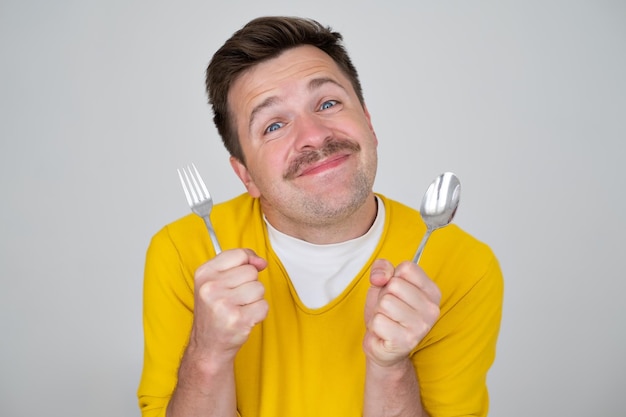 Handsome hungry young man holding fork and spoon waiting for dinner