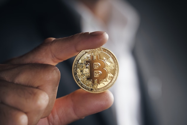 Handsome Investor Businessman in black suit holding a golden bitcoin on dark background, trading, Cryptocurrency, Digital virtual currency, alternative finance and investment Concept.