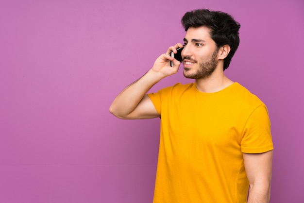 Handsome over isolated purple wall keeping a conversation with the mobile phone