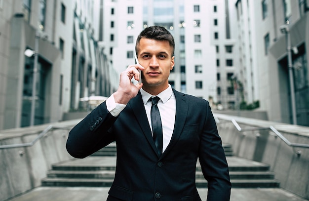 Handsome joyful businessman in smart black suit and tie talking on the phone