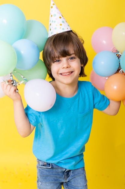 Handsome Little birthday boy in blue shirt and hat with balloons yellow background happy birthday