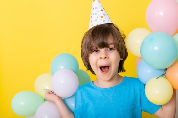 Handsome Little birthday boy in blue shirt and hat with balloons yellow background happy birthday