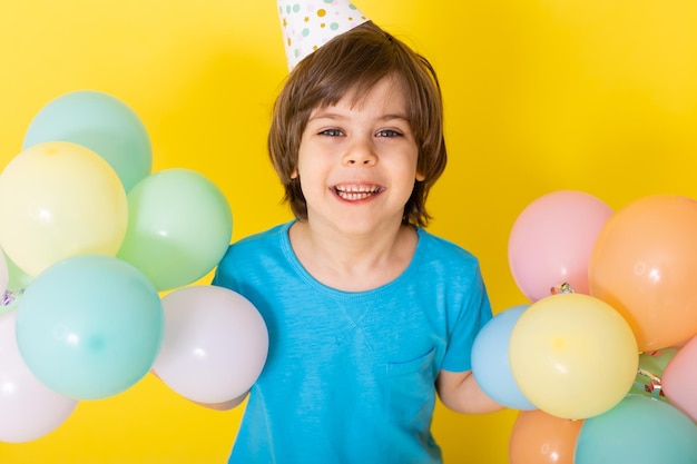 Handsome Little birthday boy in blue shirt and hat with balloons yellow background happy birthday