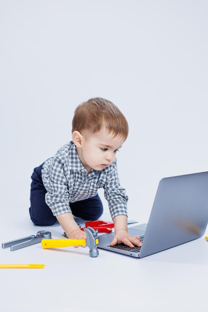 A handsome little boy 23 years old in a shirt on a white background is looking at a laptop A child is playing with a portable laptop