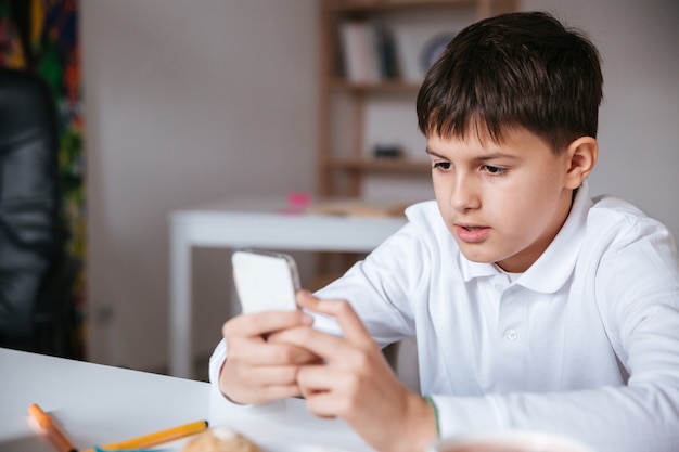 Handsome little boy sitting at the table and using mobile phone