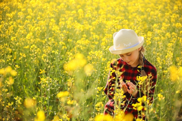 Handsome little girl with hat naturalist scientist explores plant life and insect life in rapeseed f