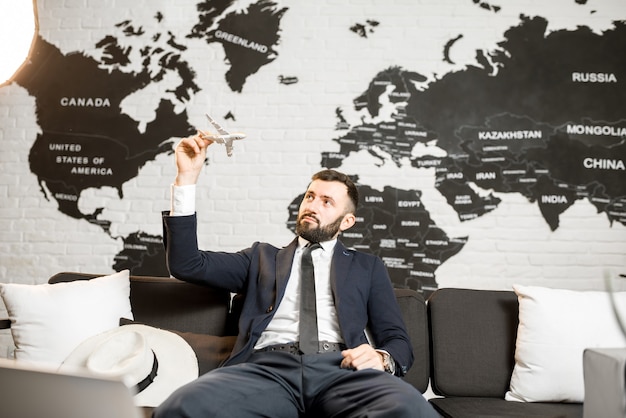 Handsome male agent playing with toy airplane at the travel agency office with world map on the background