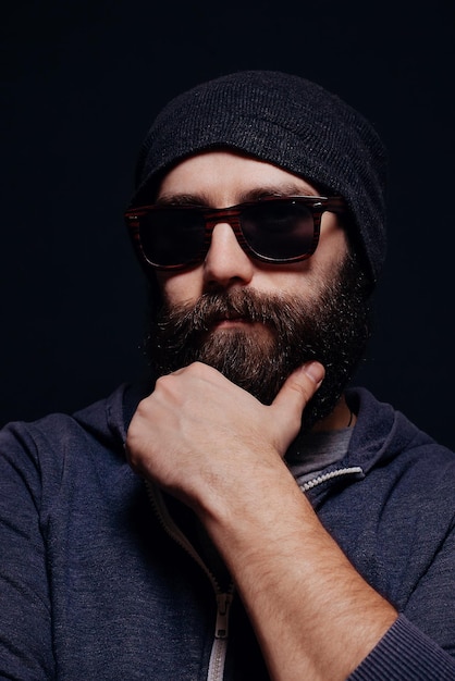 Handsome male big beard in glasses and hat studio shot on black background looking directly at the camera