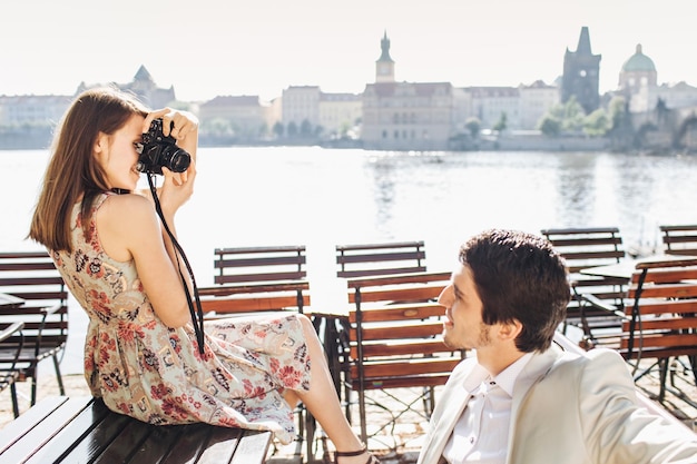 Handsome male poses at camera being in good mood spends free time with girlfriend who photographs him wonderful landscape in background Female and male active tourists go sightseeing together