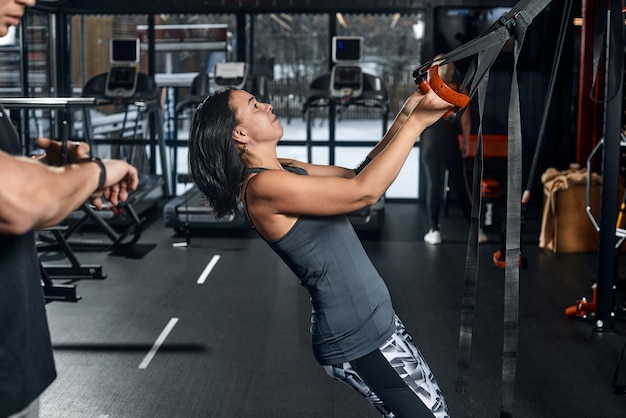 Handsome male trainer with athletic body helps girl client to perform proper exercises on the simulator The concept of training with a coach man