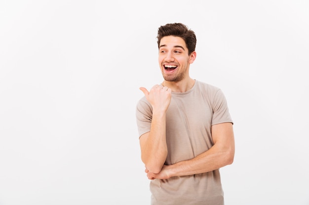 Handsome man 30s with brown hair wearing beige t-shirt gesturing finger aside on copyspace, isolated over white wall