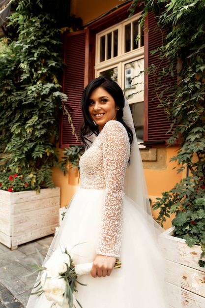 Handsome man or african American groom hugging pretty girl or cute bride with beautiful blond hair in white sexy wedding dress outdoors on blurred city street background