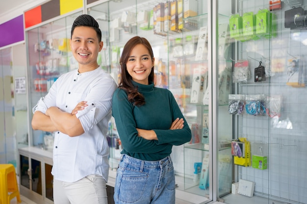 Handsome man and beautiful woman smiling with crossed hands near cell phone accessories display case