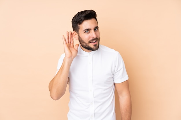 handsome man on beige listening to something by putting hand on the ear