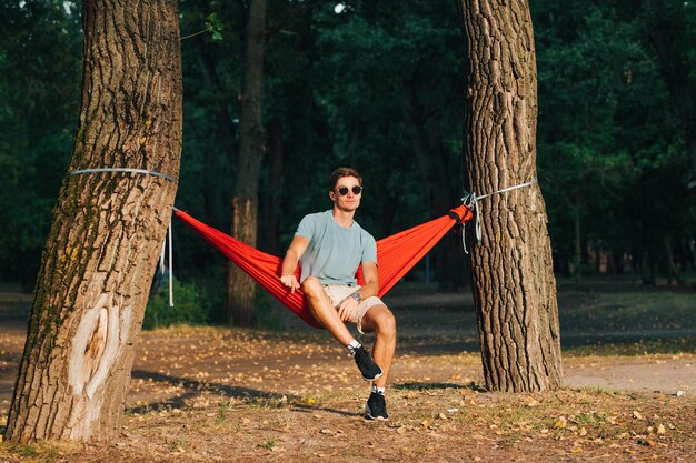 Photo handsome man in bright stylish clothes sits in a hammock in nature in the evening at sunset