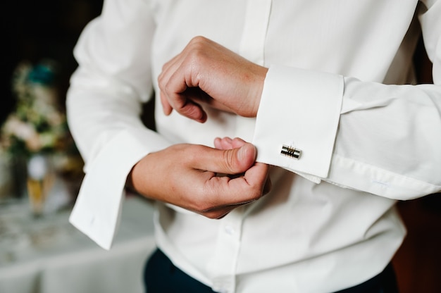 Photo handsome man buttoning cufflinks on white shirt. groom's elegant male gold cufflink. wedding preparation morning of the groom.