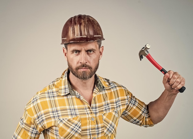 Handsome man carpenter in construction safety helmet and checkered shirt on building site with hammer maintenance