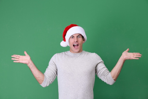 Handsome man in Christmas hat on color background