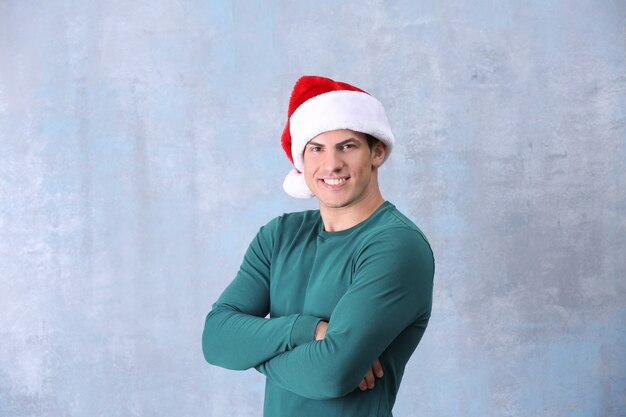 Handsome man in Christmas hat on color background