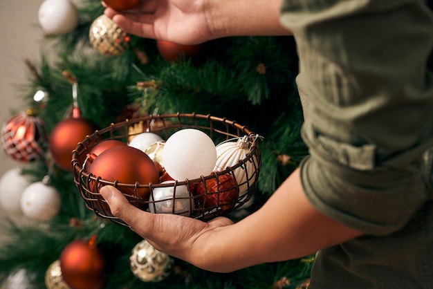 Handsome man decorating christmas tree with baubles and looking at camera at hom