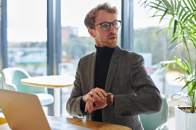 Handsome man in formal suit checks the time on wrist watch waits for business partner at meeting