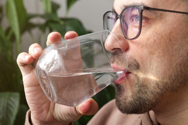 Handsome man in glasses drinking fresh glass of water at home