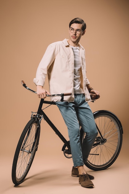 Photo handsome man in glasses standing near bike on beige background