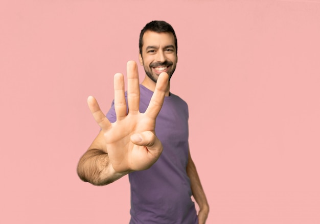 Handsome man happy and counting four with fingers on isolated pink background