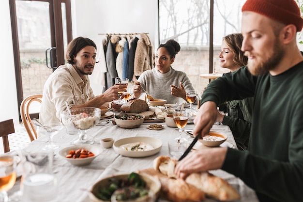 Handsome man in hat with beard sitting at the table thoughtfully cutting baguettes