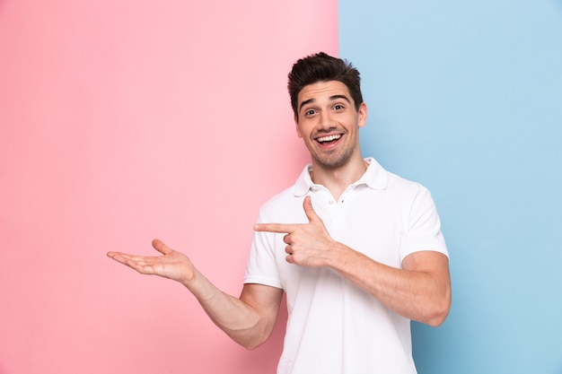 handsome man having stubble pointing fingers aside at copyspace, isolated over colorful wall